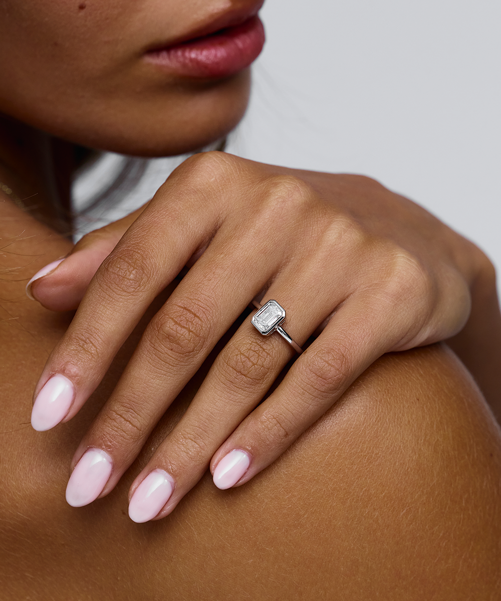 Emerald-cut diamond solitaire ring with pink manicured nails on hand
