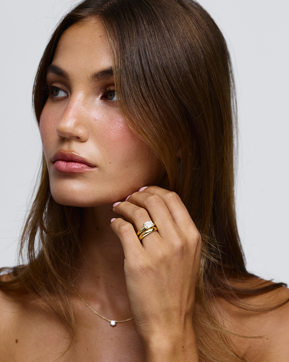 Lifestyle shot of horizontal emerald cut diamond ring stacked with plain gold band