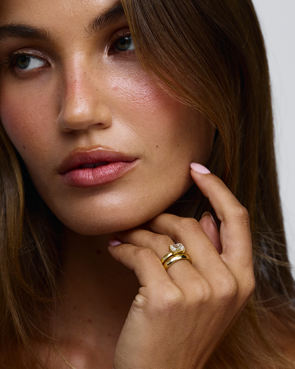 Woman wearing east west emerald cut diamond ring paired with simple gold wedding band