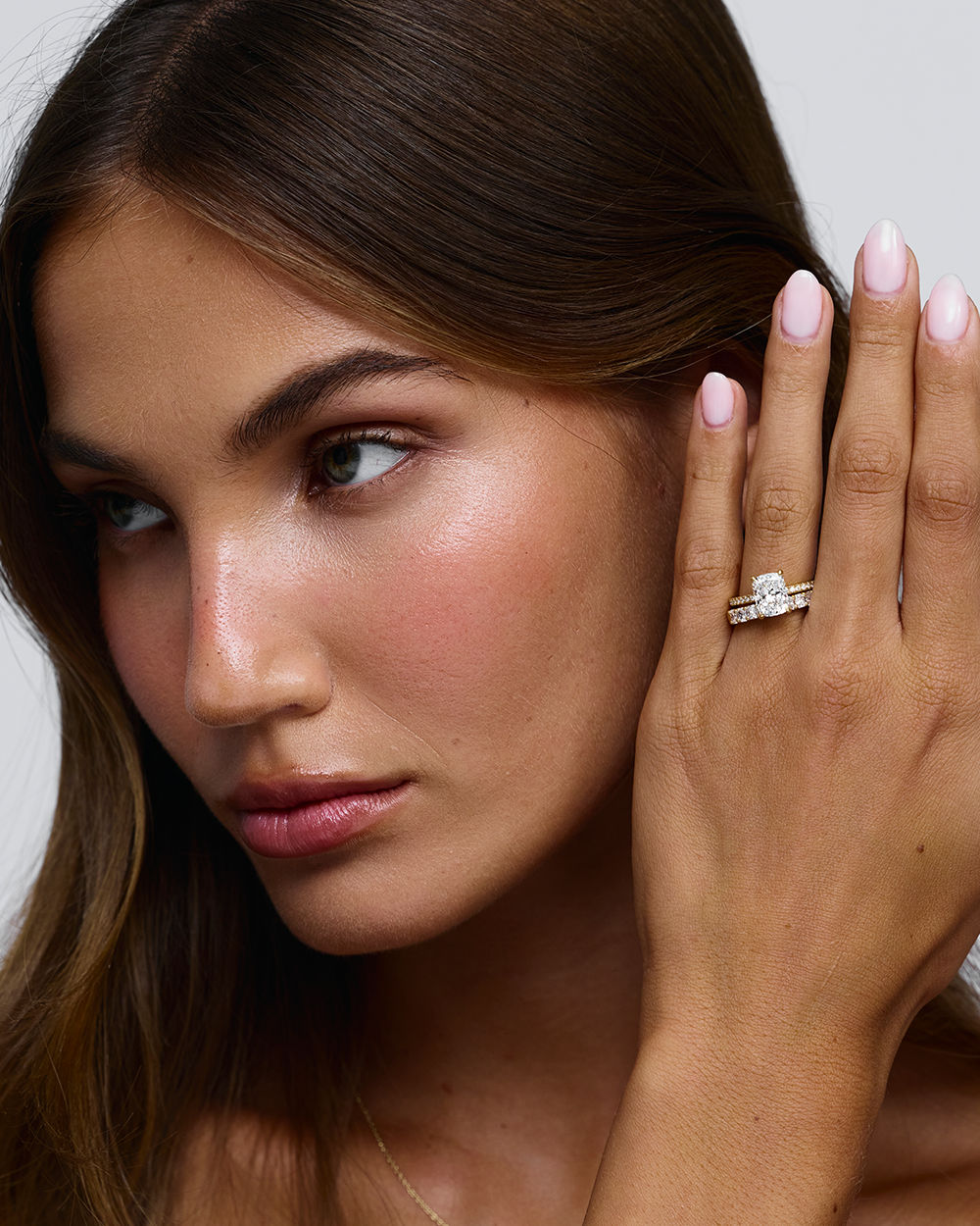 Woman touching temple while displaying 18ct yellow gold cushion cut solitaire ring with full diamond band