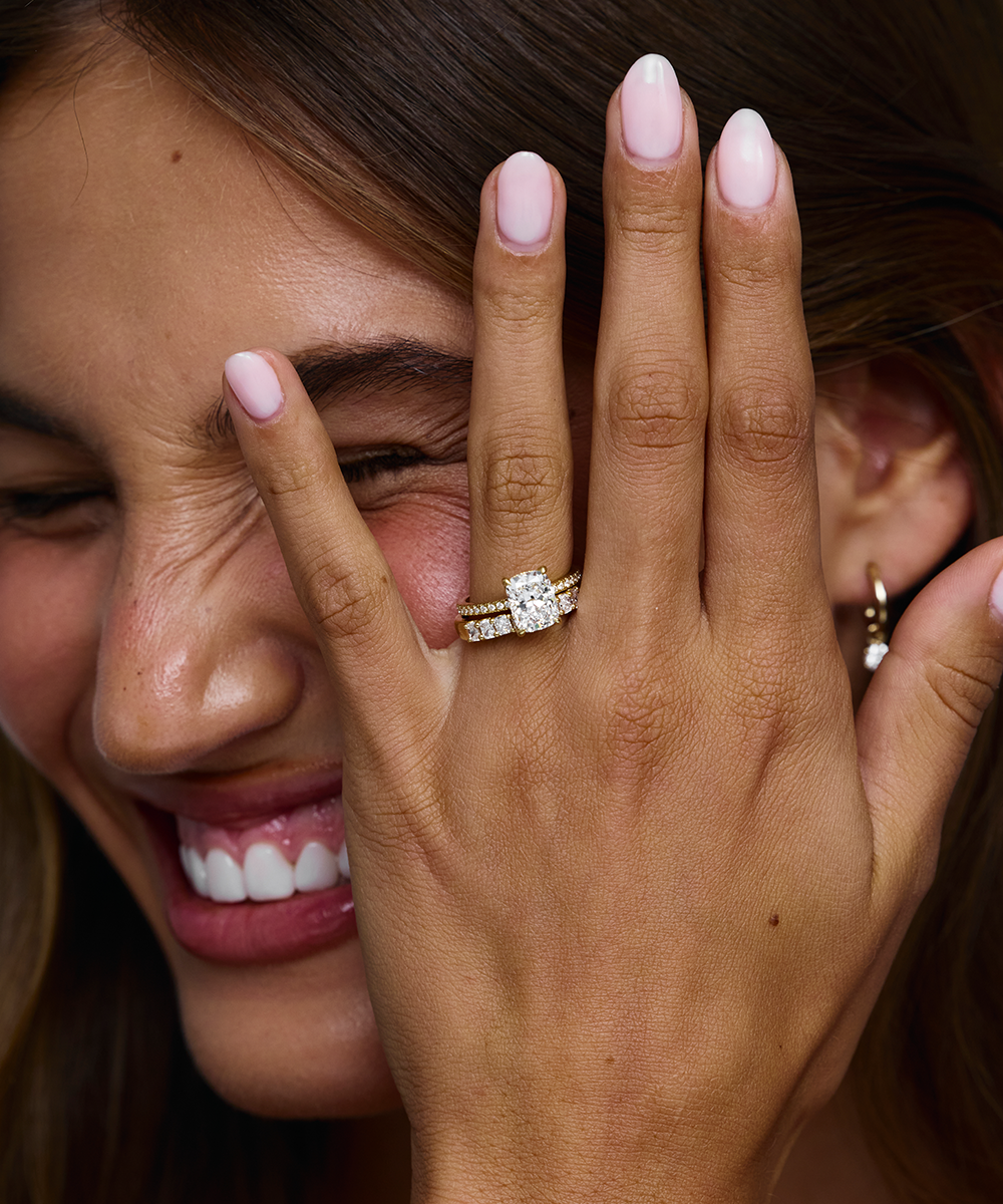 Smiling woman showing 18ct yellow gold cushion cut engagement ring with diamond band on finger