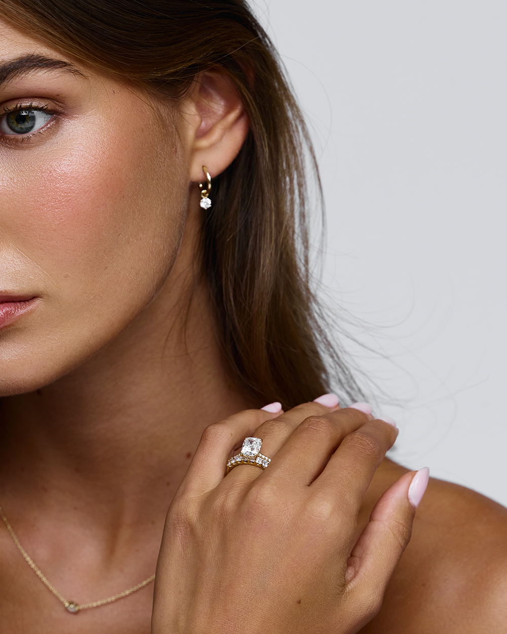 Woman wearing 18ct yellow gold solitaire engagement ring near collarbone with diamond hoop earring