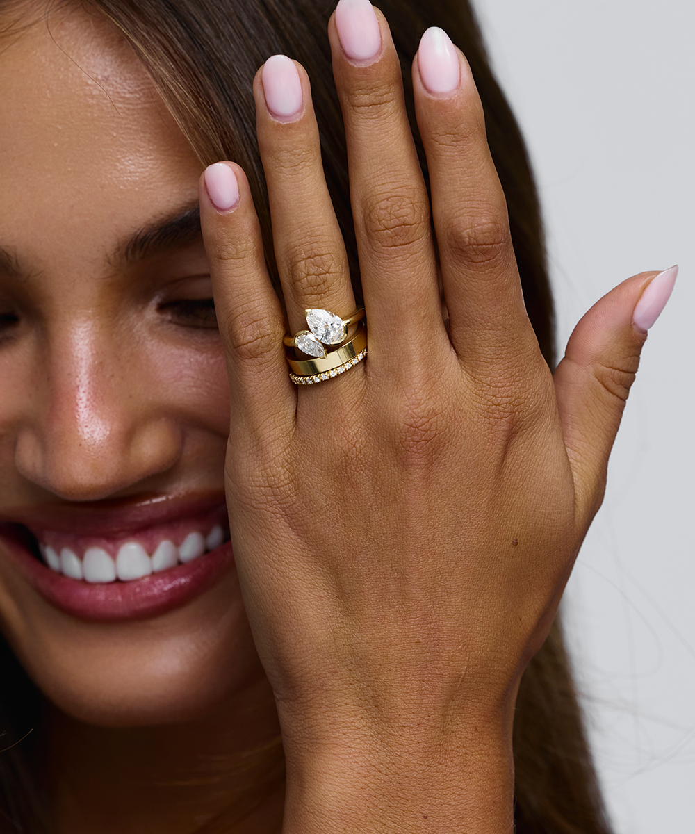 Three stacked pear shaped diamond rings on woman's finger against light background