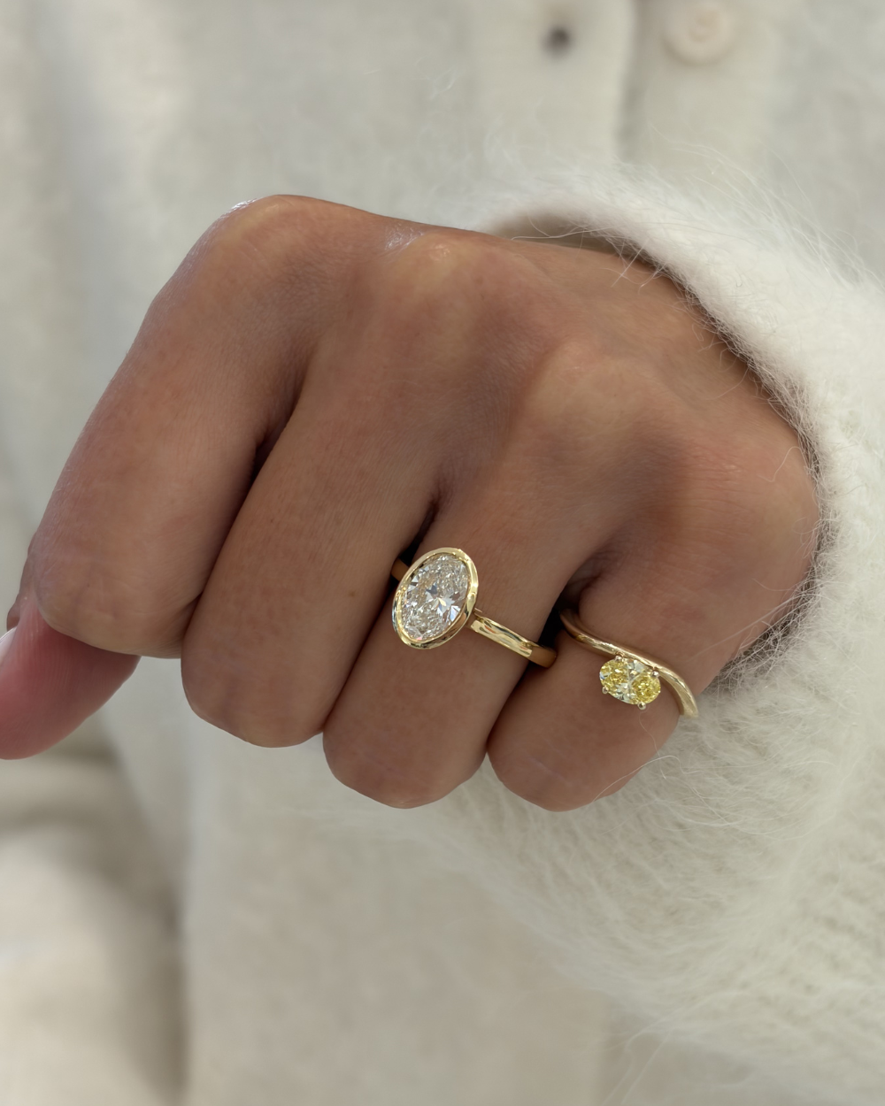 18ct yellow gold oval diamond bezel ring worn on index finger with fluffy white sweater background
