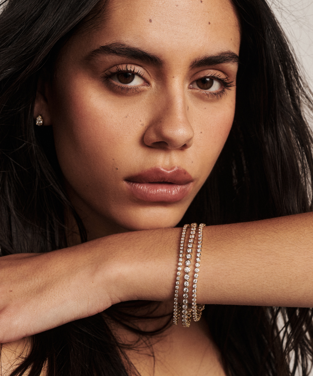 Model wearing layered yellow gold tennis bracelets with matching stud earrings