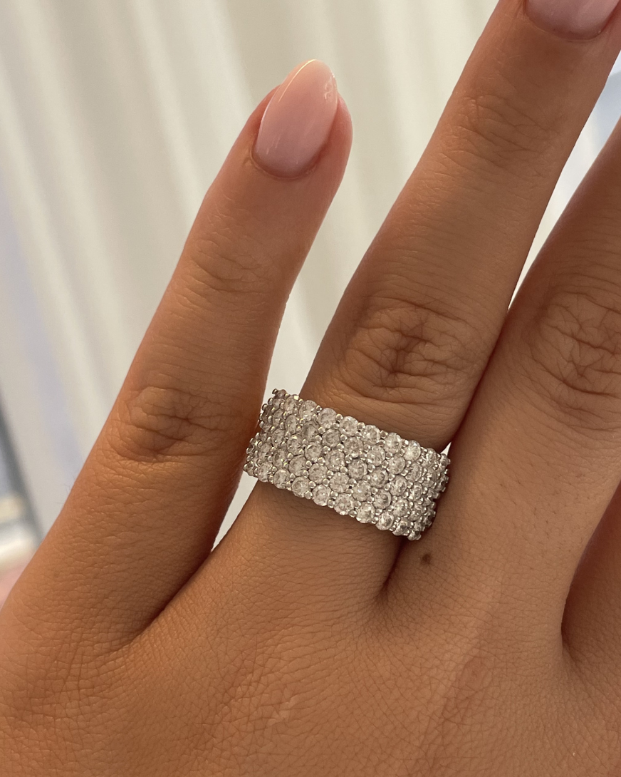 Silver ring with diamonds on a person's finger against a neutral background