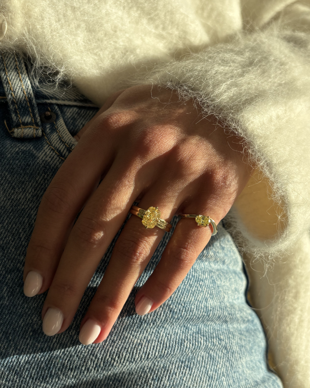 Layered yellow diamond rings on denim with knit sweater sleeve