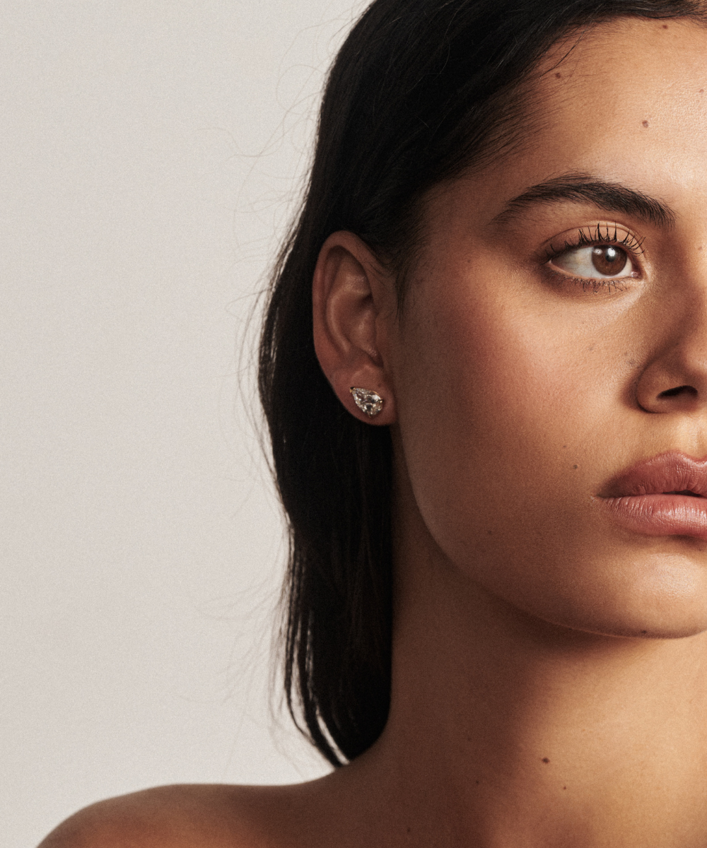 Close up of woman's ear wearing gold pear cut diamond stud with natural lighting