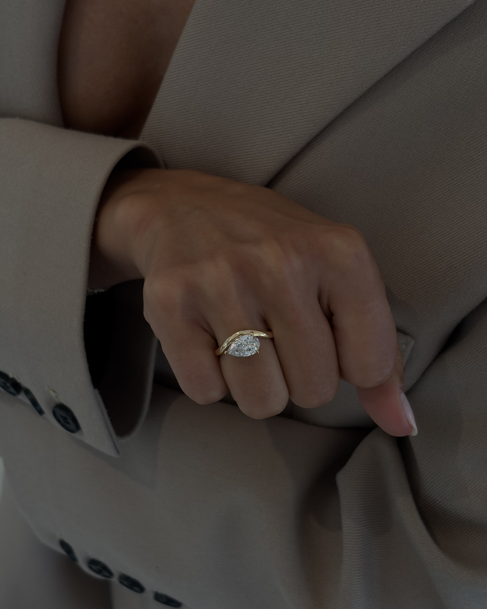 Woman wearing Lucie pear diamond engagement ring on hand with textured suit sleeve