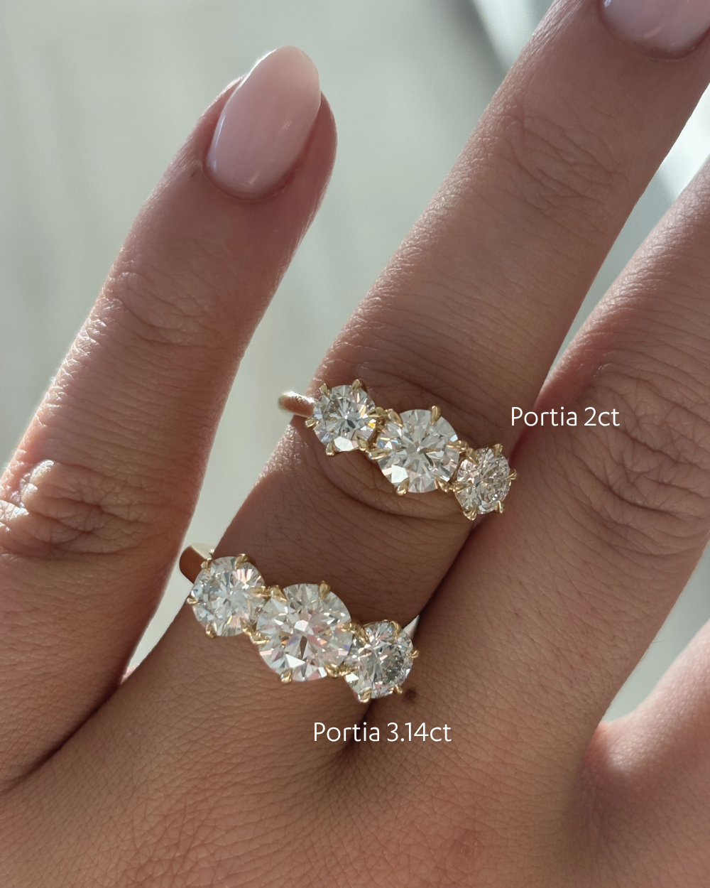 18ct yellow gold Portia trilogy engagement rings side-by-side on fingers showing 2ct and 3.14ct lab grown diamond sizes