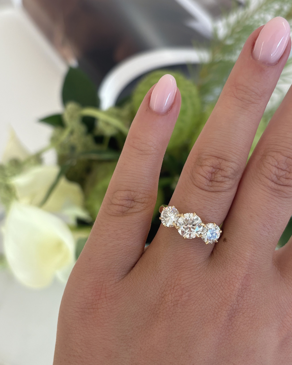 Close-up of woman wearing Portia trilogy ring with pink manicured nails showing real-life wearability of 18ct yellow gold