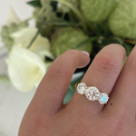 Portia trilogy engagement ring worn on finger with white calla lilies highlighting sparkle of round lab grown diamonds