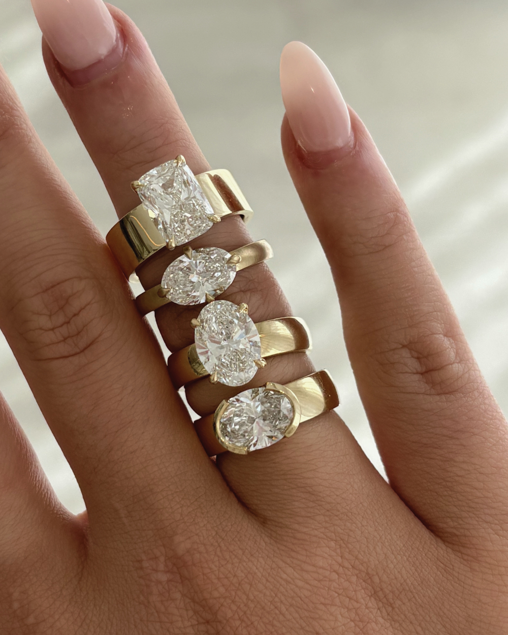 Four 18ct yellow gold solitaire rings with oval and cushion lab-grown diamonds on hand