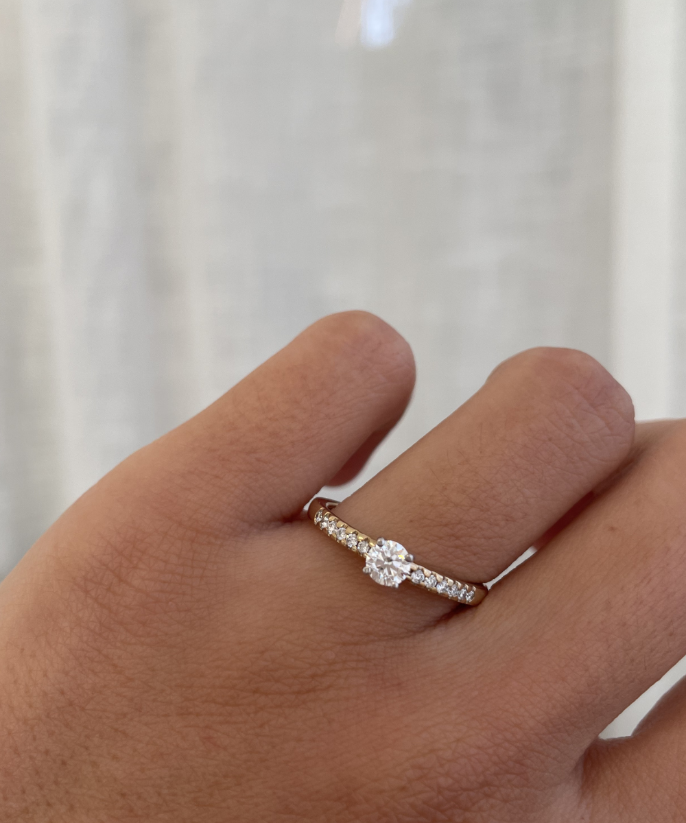 Hand wearing a diamond ring against a neutral background