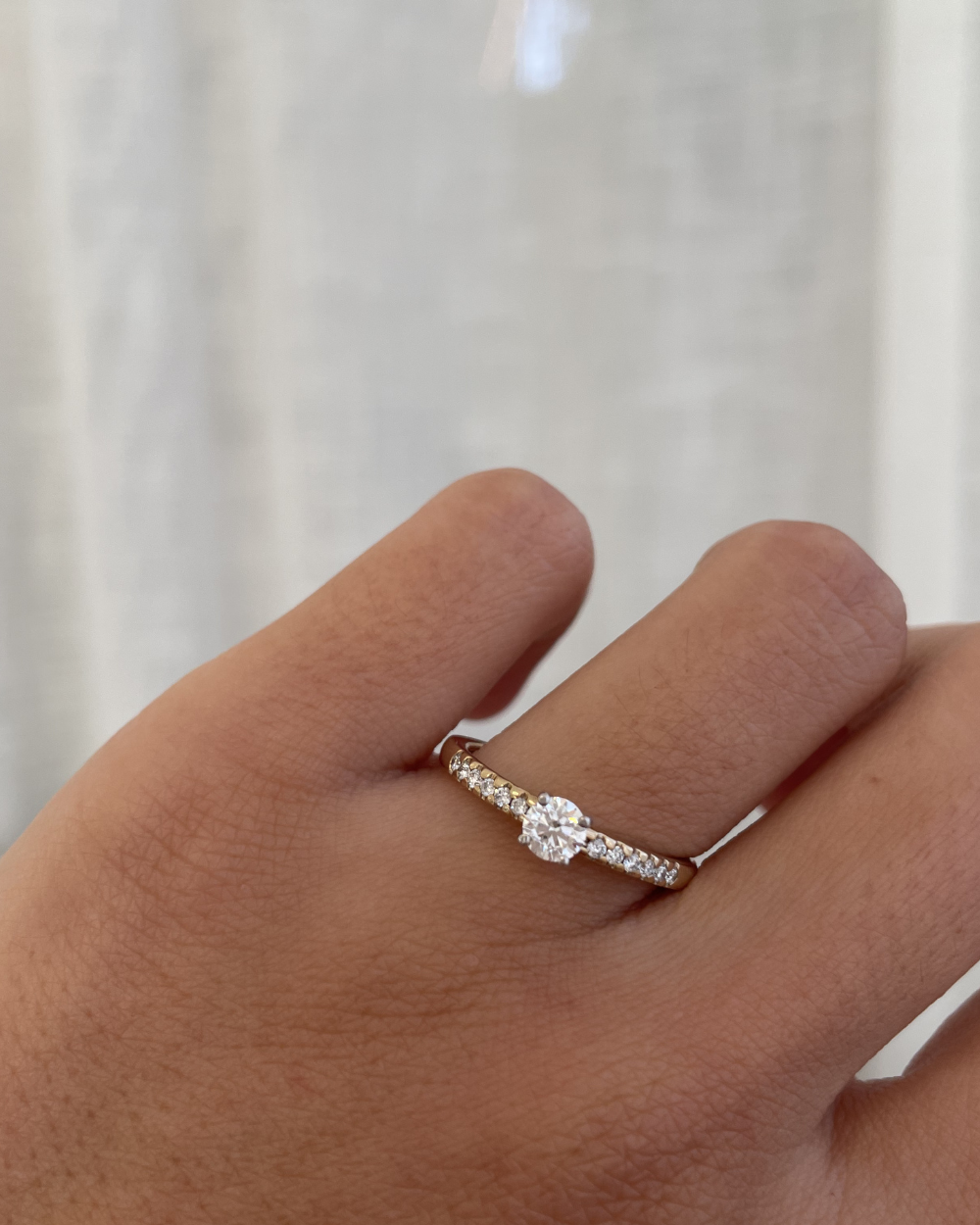 Hand wearing a diamond ring against a neutral background