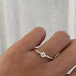 Hand wearing a diamond ring against a neutral background