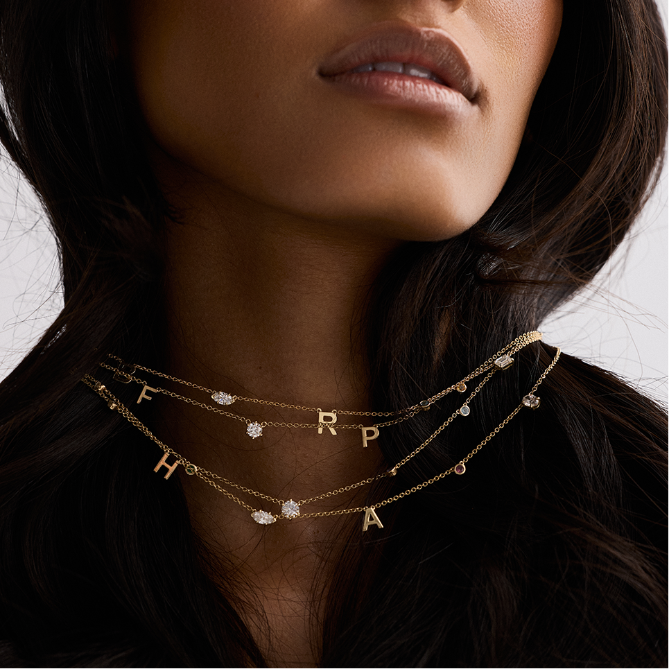 Woman wearing gold necklaces with letter pendants against a neutral background