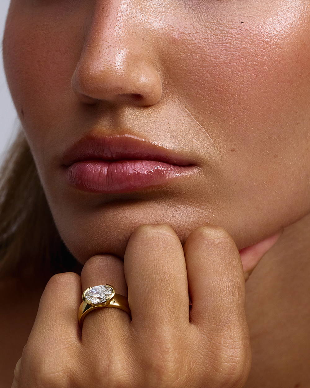 Close-up of Arabella east-west oval diamond ring on finger against jawline