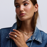 Gold teardrop earring layered with denim jacket and jewelry