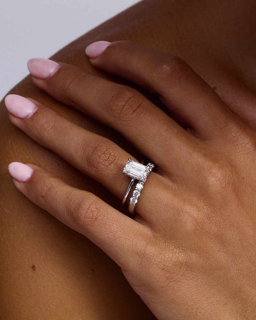 Emerald cut solitaire ring stacked with diamond wedding band profile view