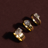 Three 18ct yellow gold engagement rings with cushion, oval, and emerald cut diamonds on burgundy background