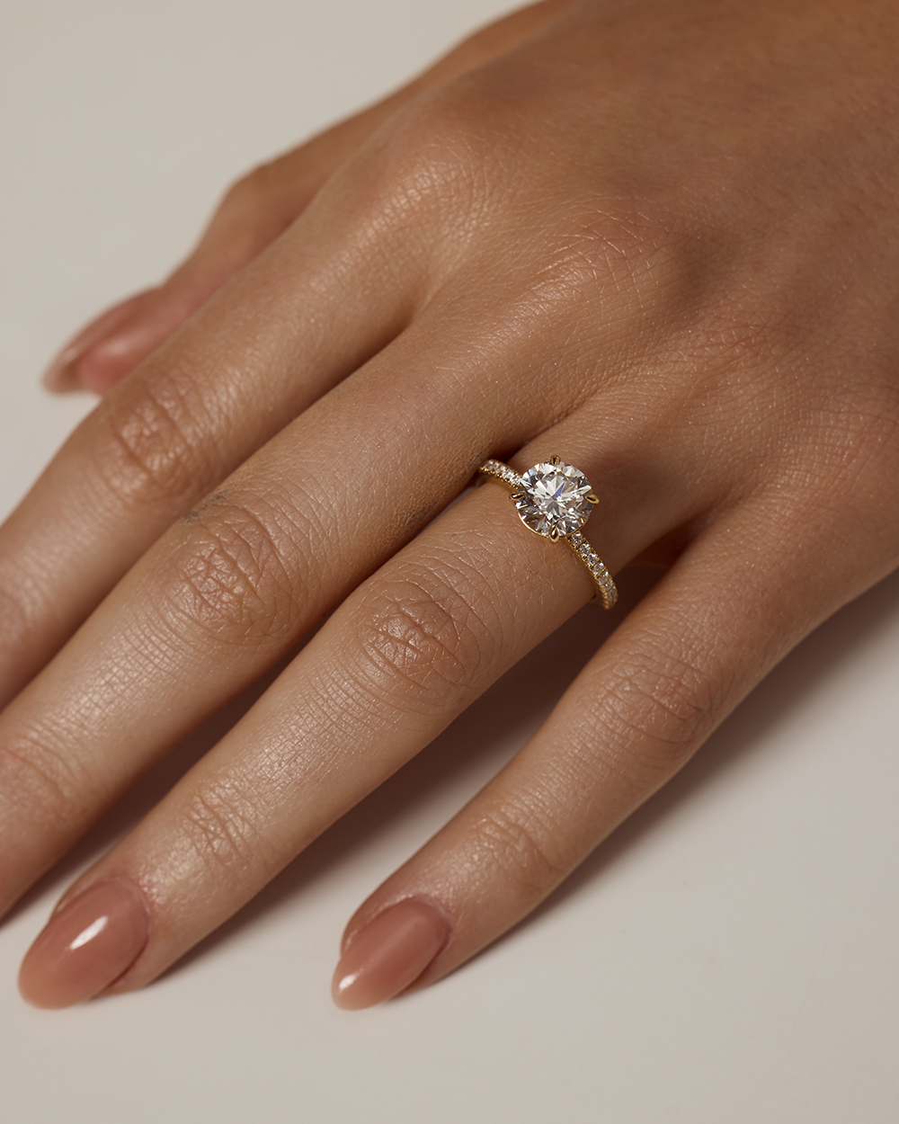 Close-up of a hand wearing a diamond ring on a neutral background