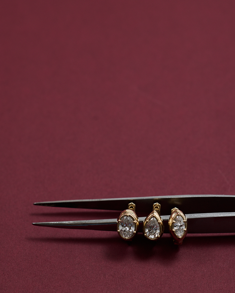 Two gold earrings on a black fork against a maroon background
